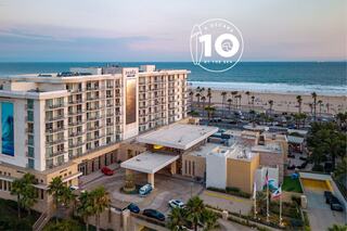 A beachfront hotel with modern architecture, palm trees, and ocean views, celebrating a decade of service with a logo feature.