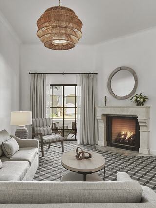 A stylish living room features a cozy fireplace, modern furniture, a patterned rug, and a chic woven chandelier above.