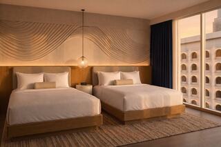 A modern hotel room features two comfortable beds, warm lighting, and an elegant design, with large windows offering a view outside.