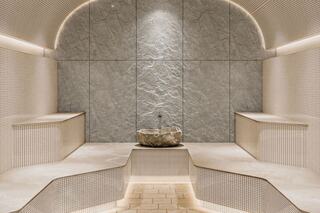A serene, minimalist spa area featuring smooth stone surfaces, soft lighting, and a central stone basin, inviting relaxation and tranquility.