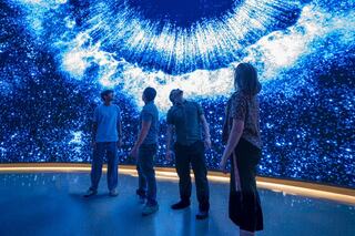 A group of four individuals gazes upwards at a stunning, starry digital display resembling a cosmic scene.