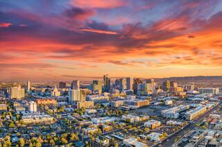 A vibrant city skyline glows under a dramatic sunset, with colorful clouds casting shades of orange and pink over the bustling urban landscape.
