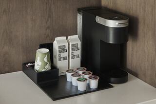 A sleek coffee maker sits beside boxed water and flavored coffee pods, arranged neatly on a dark tray with a decorative cup.