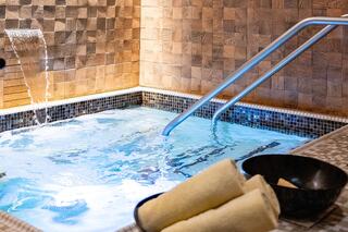 A serene spa area features a bubbling jacuzzi with a soothing waterfall, complemented by neatly arranged towels and a sleek design.