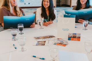Three women at a table review menus, surrounded by water glasses and promotional materials, suggesting a meeting or event at a hotel.