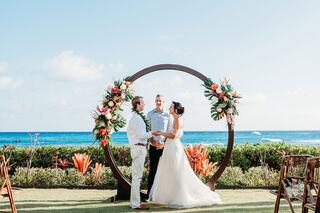 A bride and groom share a tender moment under a decorative gazebo, surrounded by lush vineyards and elegant floral arrangements.