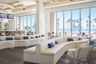 Bright, modern lounge area features curved white seating, blue accents, and large windows offering ocean and palm tree views.