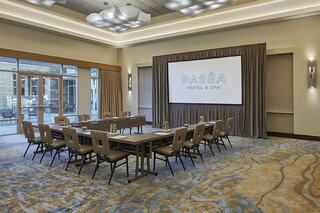 A modern conference room features a large screen, several tables arranged for a meeting, and stylish seating, with natural light streaming in.