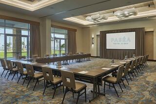 A modern conference room features U-shaped seating, large windows, and a screen displaying "PASÉA HOTEL & SPA," with a view of palm trees outside.