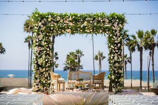 A floral arch framed by palm trees overlooks a serene ocean view, with elegant chairs set for a romantic ceremony.