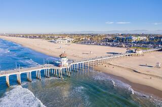 A serene beach scene features a long pier stretching into the ocean, with golden sand, gentle waves, and palm trees lining the shore.