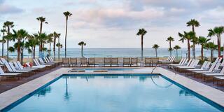A serene poolside scene with lounge chairs, palm trees, and an ocean view under a cloudy sky. Perfect for relaxation and leisure.