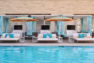 A stylish poolside area features lounge chairs with vibrant orange and turquoise decor, shaded by large umbrellas, perfect for relaxation.
