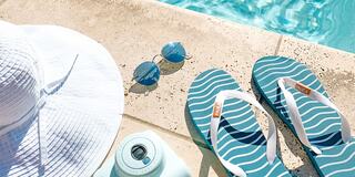 A sunhat, stylish sunglasses, and beach flip-flops rest on a poolside, inviting a day of relaxation and fun by the water.