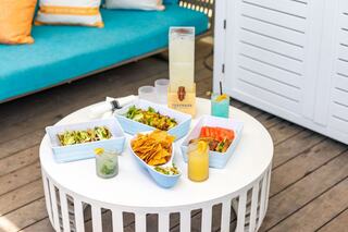 A woman sits by the pool in a beige bikini, holding a drink with orange slices, enjoying a sunny day. A relaxed atmosphere surrounds her.
