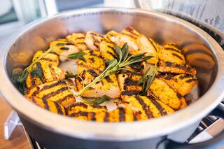 Grilled salmon fillets are arranged in a pot, garnished with fresh herbs, showcasing golden grill marks and a delicious appearance.