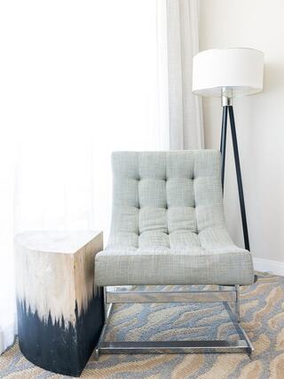 A modern, tufted gray chair sits beside a stylish side table and a tripod lamp, enhancing a tranquil, minimalist interior space.