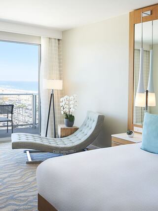 A modern hotel room featuring a sleek lounge chair, a sunny balcony with ocean views, and stylish decor for a comfortable stay.