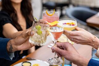 Cheers with a variety of colorful cocktails, showcasing a festive gathering among friends at a stylish dining setting.