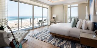 A modern beachfront hotel room features large windows, elegant furnishings, and a cozy ambiance, overlooking the ocean and sandy shore.