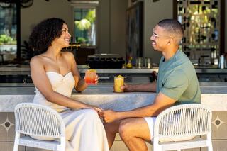 A couple enjoys drinks at a stylish bar, smiling and holding hands, exuding joy and connection in a vibrant setting.