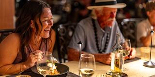 A joyful couple enjoys a meal together at a bright table, surrounded by vibrant tropical plants and flowers.