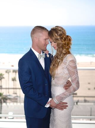 A happy couple shares a romantic moment by the beach, dressed elegantly for their wedding, surrounded by a beautiful ocean backdrop.