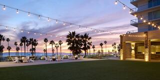 A serene outdoor space with lounge chairs, palm trees, and warm sunset hues, illuminated by string lights, perfect for relaxation.