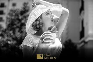 A woman in a wide-brimmed hat holds a drink, gazing thoughtfully into the distance, radiating a sense of summer elegance.