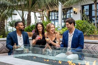 Four friends enjoy cocktails around a firepit, surrounded by lush greenery and a stylish outdoor setting, sharing laughter and good times.