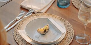 A beautifully set table features a single oyster on a pale plate, accompanied by elegant cutlery and a glass of wine, creating a refined dining atmosphere.