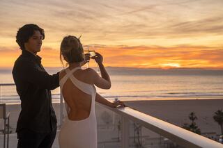 A couple toasts with drinks at sunset, overlooking a serene beach, capturing a moment of intimacy and beauty.