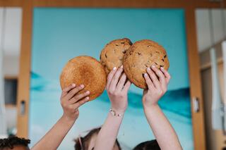 Hands raise three delicious cookies against a colorful background, showcasing a shared moment of joy and indulgence.