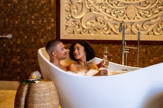 A couple shares a romantic moment in a luxurious bathtub, surrounded by bubbles and elegant decor, enjoying each other's company.