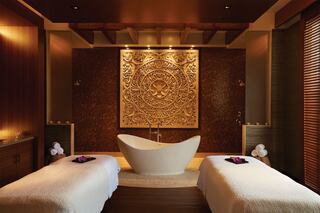 A serene spa room featuring a sculptural wall, a sleek bathtub, and massage tables, creating a tranquil atmosphere for relaxation.