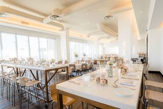 A bright and spacious event space with elegantly set tables, wooden accents, and large windows allowing natural light to fill the room.