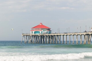 A colorful pier with a red rooftop stands over gentle waves, under a clear sky, inviting visitors to enjoy the seaside view.
