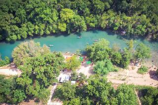 A serene river winds through lush greenery, with people kayaking and relaxing along sandy banks, creating a peaceful natural escape.