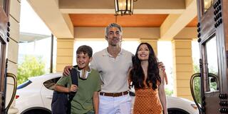 A happy family stands together at an entrance, smiling. A boy in casual attire holds headphones, while adults exude warmth and joy.