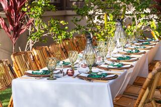 A beautifully set outdoor dining table with bamboo chairs, elegant glassware, and lush greenery in the background, creating a vibrant ambiance.