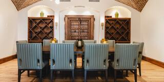A stylish dining room featuring a long table flanked by green chairs, wooden shelves for wine, and a rustic arched ceiling.
