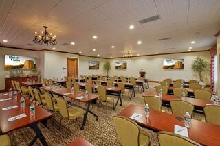A well-equipped conference room with rows of tables and chairs, screens displaying a hotel logo, and plants for a welcoming atmosphere.