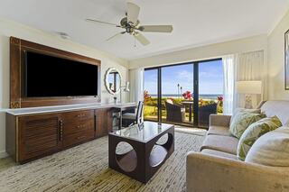 A bright living space features a comfortable couch, modern furniture, a large TV, and a beautiful view of the outdoors through glass doors.