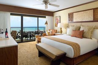 A serene hotel room features a large bed, stylish decor, and a balcony with ocean views, creating a relaxing atmosphere.