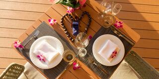 A beautifully set table for two, adorned with flowers, elegant glassware, and a heart-shaped decoration, creates a romantic atmosphere.