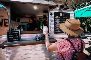 A woman in a straw hat orders a treat from a vibrant food truck, while a friendly staff member assists her with a smile.