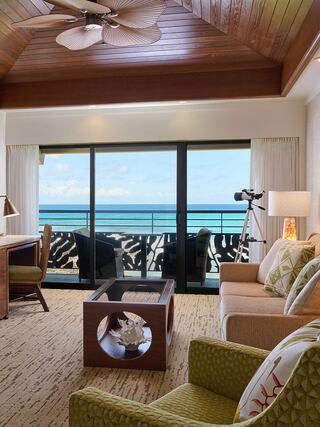 A cozy living area features stylish furniture, large windows with ocean views, and tropical decor, enhancing a relaxing atmosphere.