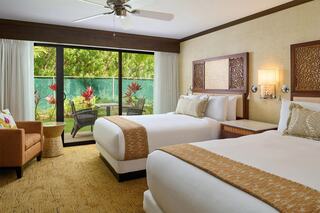 A cozy hotel room features two beds, a comfortable chair, and sliding glass doors opening to a vibrant garden view.