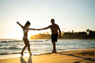A couple joyfully dances along the beach at sunset, capturing a moment of connection and happiness against a picturesque backdrop.