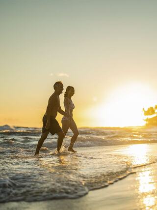 A couple walks hand in hand along the beach, enjoying the sunset and the warm waves lapping at their feet. Pure joy and connection.